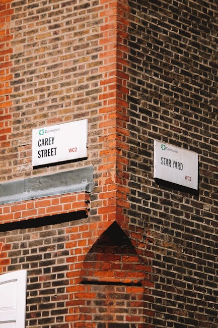 A black and white photograph of a street view in Camden Town, showcasing a row of storefronts with large window displays and signage, including a guitar shop and a bookshop. The pavement in front of t