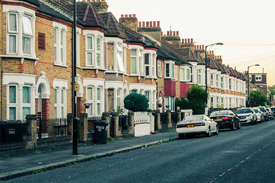 A row of terraced Victorian-style houses with brick facades and white window frames lining a residential street in Kentish Town during daylight. Several houses have black metal fences and small front