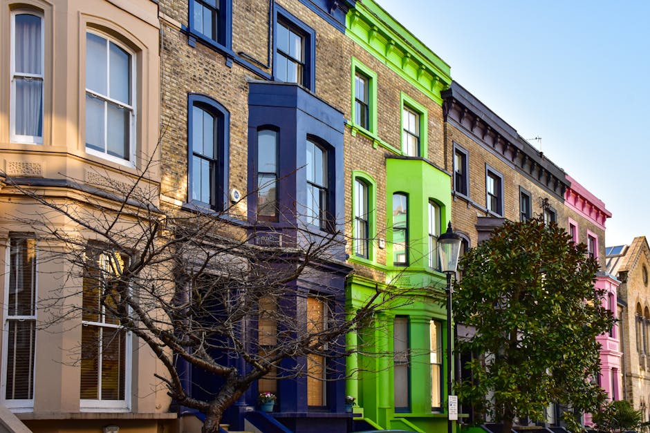 A row of terraced Victorian-style houses with brick facades and white window frames lining a residential street in Kentish Town during daylight. Several houses have black metal fences and small front